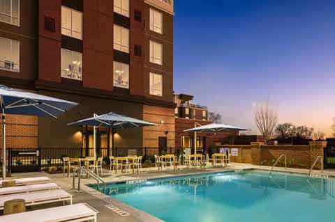 Evening pool view with illuminated brick building, yellow umbrellas, and lounge seating area