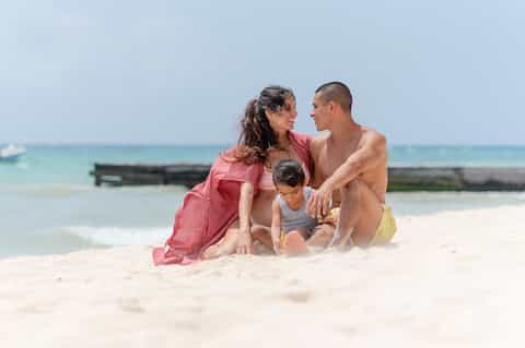 Family of three enjoying the beach together in shallow turquoise water on sunny day