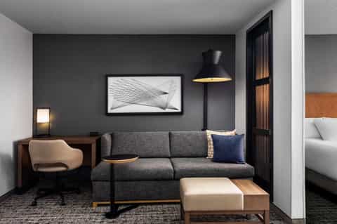 Contemporary hotel room with dark accent wall, gray sofa, desk, and modern furnishings