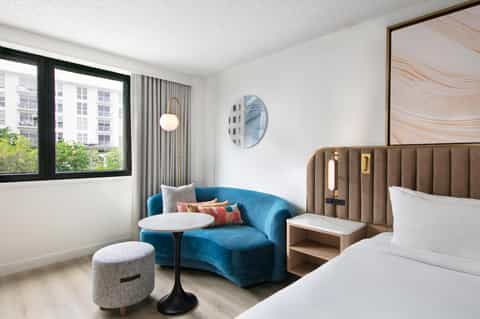Contemporary hotel room with blue accent chair, bed, and city views