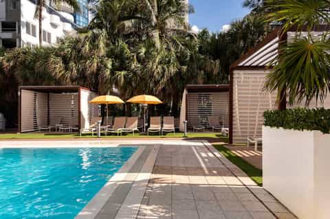 Resort pool with yellow umbrellas, palm trees, privacy screens, and manicured lawn areas