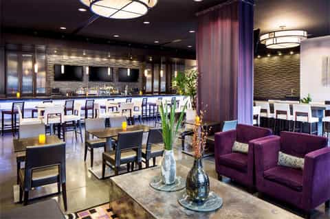 Contemporary hotel bar and lounge with purple seating, marble countertop, and ambient lighting