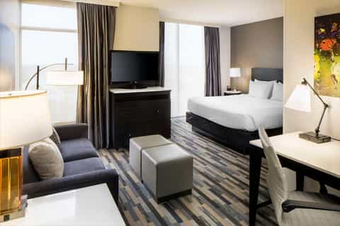 Modern hotel room with queen bed, flat-screen TV, gray accents, and contemporary furnishings