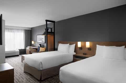 Contemporary hotel guest room with two queen beds, dark accent wall, wooden headboards, and modern minimalist decor