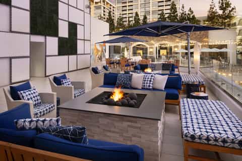 Rooftop lounge with fire pit, blue and white seating, umbrellas, and city views at dusk