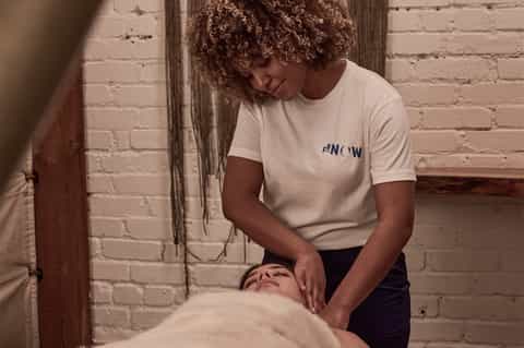 Spa therapist performing massage treatment on client wearing NOW branded shirt