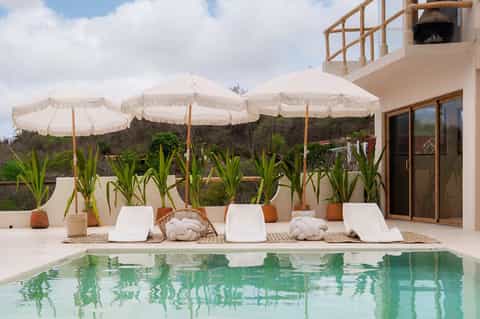 Resort pool area with white umbrellas, lounge chairs, and modern architectural building