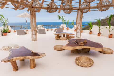 Coastal lounge area with wooden pergola, woven hanging lights, ocean view, and modern wood seating