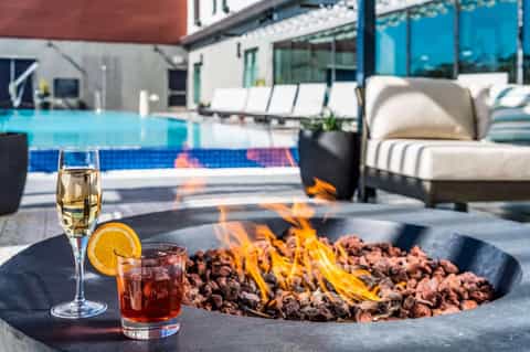 Outdoor fire pit with cocktails and pool lounge area with seating and blue water background