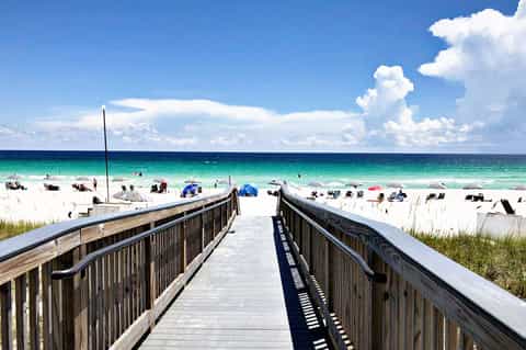 Wooden boardwalk leading to pristine turquoise ocean beach with white sand and colorful umbrellas