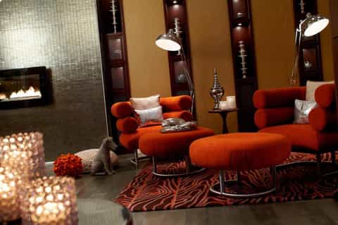 Luxury lounge with orange velvet seating, fireplace, pendant lighting, and ornate wall panels