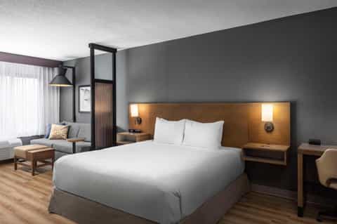 Contemporary hotel bedroom with wooden headboard, white bedding, modern lighting, and gray accent wall