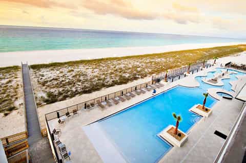 Beachfront resort with blue pool, lounge chairs, and white sand beach with turquoise ocean