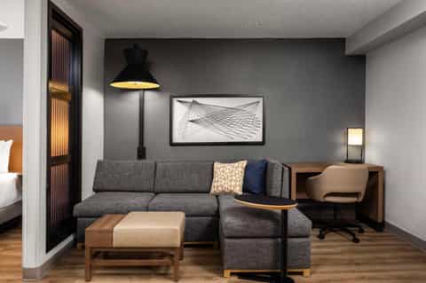 Modern hotel suite living area with gray sofa, wood furniture, and contemporary wall art