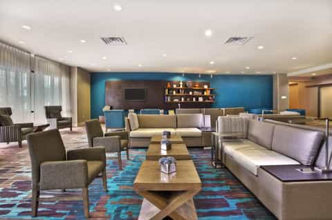 Modern hotel lounge with blue accent wall, gray upholstered seating, wood tables, and contemporary décor
