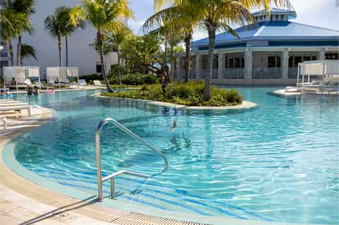 Resort pool with palm trees, white lounge chairs, and white colonial-style clubhouse building