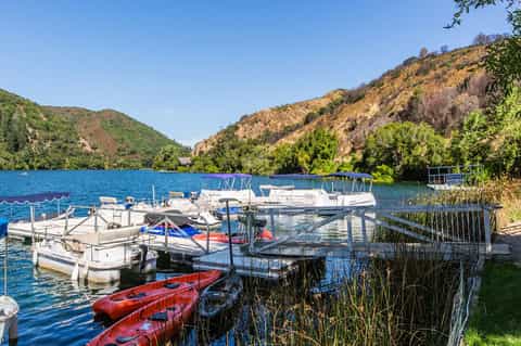 Scenic mountain lake with docked boats, kayaks, forested hills, and autumn foliage