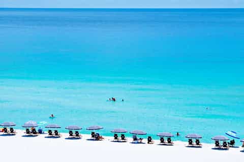 Aerial view of white sand beach lined with purple umbrellas and lounge chairs along turquoise water