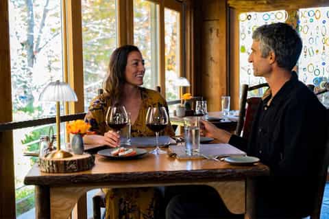 Couple dining at restaurant table with forest view and wine glasses