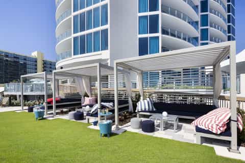Modern curved hotel building with rooftop lawn area, pergolas, striped seating, and architectural balconies