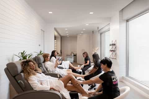 Spa pedicure area with multiple clients receiving foot treatments in modern white lounge chairs