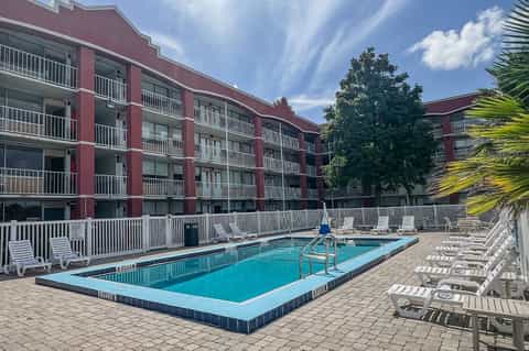 Resort pool with turquoise water, white lounge chairs, red building, and palm trees