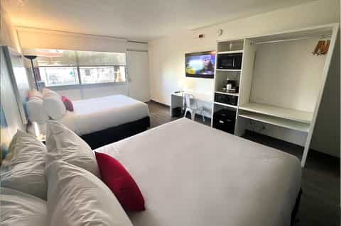 Hotel room with two queen beds, desk area, TV, and window with city views