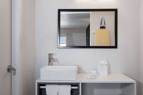 Clean bathroom vanity with white rectangular sink, black-framed mirror, and hotel amenities