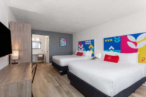Modern hotel bedroom with two queen beds, colorful abstract headboard art, desk area, and contemporary furnishings
