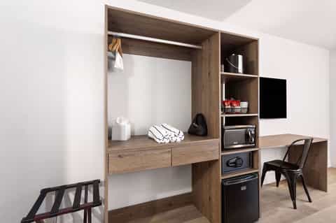 Modern hotel room wardrobe with desk, shelving, TV, and wooden cabinetry