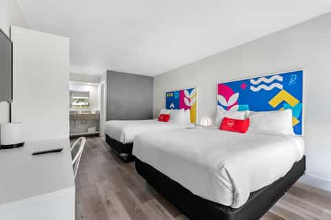 Modern hotel room with two queen beds, colorful artwork, bathroom, and contemporary furnishings