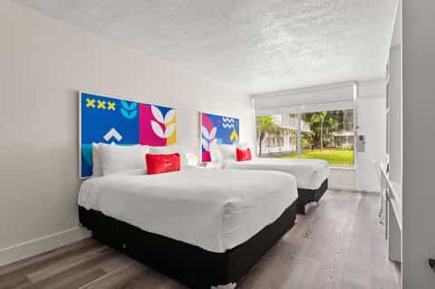 Contemporary hotel bedroom with two queen beds, colorful geometric headboard art, and palm tree courtyard view