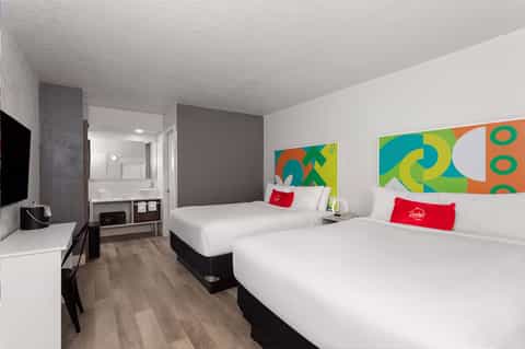 Colorful modern hotel room with two queen beds, bright artwork, and ensuite bathroom