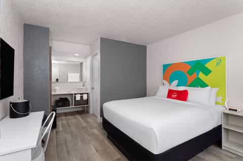 Modern hotel room with queen bed, ensuite bathroom, desk, and colorful abstract headboard art