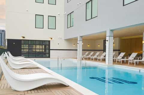Modern indoor swimming pool with loungers, white columns, glass doors opening to outdoor terrace, contemporary architecture