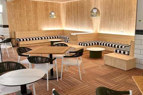 Modern lounge with wooden built-in seating, striped cushions, round tables, and pendant lighting