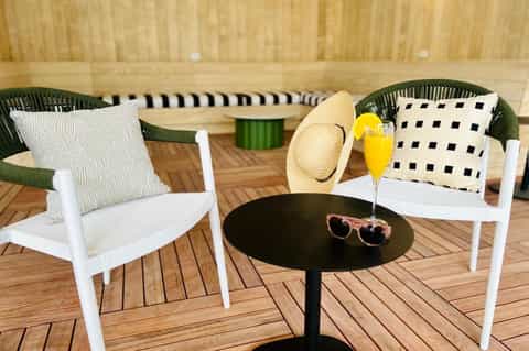 Outdoor deck seating area with white chairs, patterned pillows, and black side table with drink