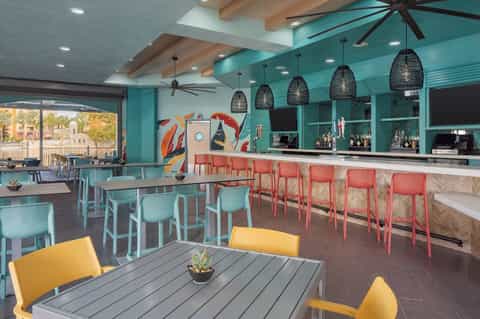 Colorful resort bar and dining area with turquoise walls, coral chairs, yellow accents, and ocean view