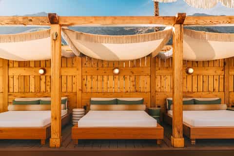Luxury beachside cabanas with wooden posts, draped white canopies, and ocean view backdrop