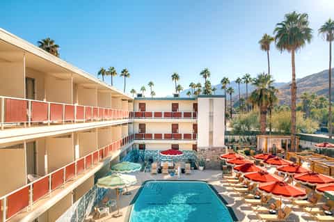 Aerial view of resort courtyard with pool, palm trees, and red umbrellas