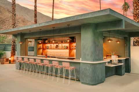Modern concrete bar with tropical sunset, palm trees, and desert mountain backdrop at dusk