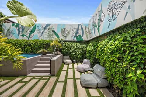 Modern poolside patio with concrete sun loungers, tropical plants, and botanical wall mural