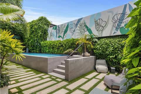 Elevated modern swimming pool surrounded by lush green landscaping and botanical wall art