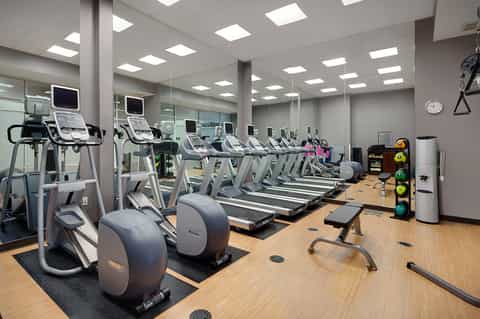 Gym with rows of cardio equipment including treadmills and stationary bikes with mirrored walls