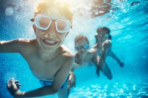 Child snorkeling underwater in bright blue pool with goggles and smile