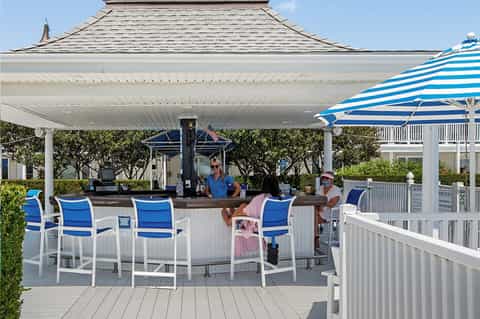 Outdoor bar with blue and white striped umbrella, bartender, and customers under a pergola