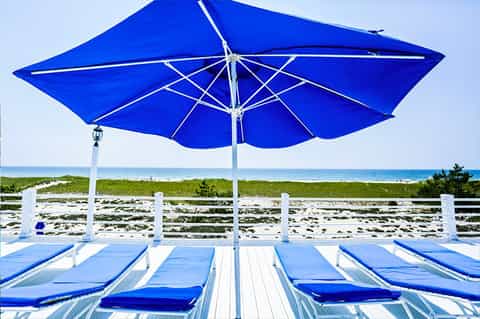 Beach lounge chairs with blue umbrella overlooking ocean, white fence, and sandy beach