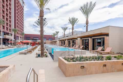 Resort pool deck with multiple pools, palm trees, lounge chairs, and pink building
