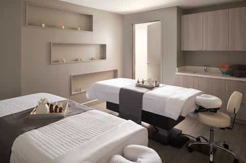 Modern spa treatment room with massage beds, recessed wall shelving, built-in bathtub, and neutral tones