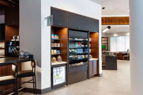 Modern hotel café with dark wood shelving, Starbucks signage, and refrigerated beverage displays